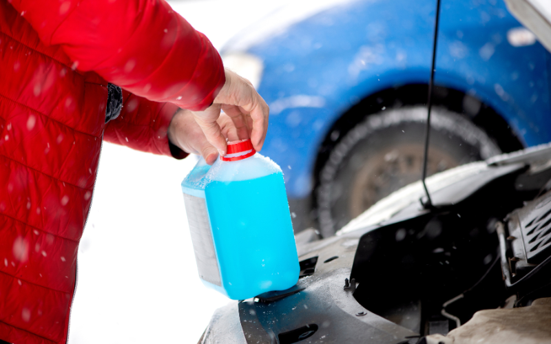 Man topping up antifreeze in car with snow in background